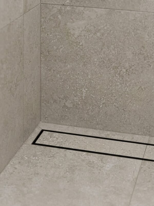 Neston Black Linear Tile Insert Drain In Shower Matte black linear tile insert drain installed along a stone-tiled shower wall