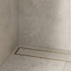 Neston Brushed Brass Linear Tile Insert Drain In Shower Brushed brass linear tile insert drain installed along a stone-tiled shower wall