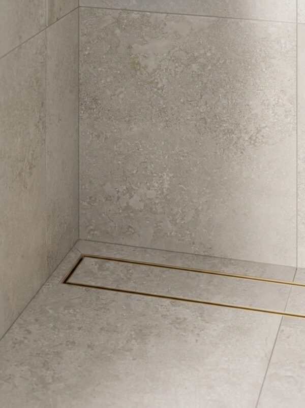 Neston Brushed Brass Linear Tile Insert Drain In Shower Brushed brass linear tile insert drain installed along a stone-tiled shower wall