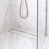 Brushed bronze linear tile insert drain installed in a white marble shower
