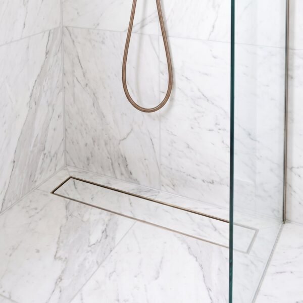 Brushed bronze linear tile insert drain installed in a white marble shower