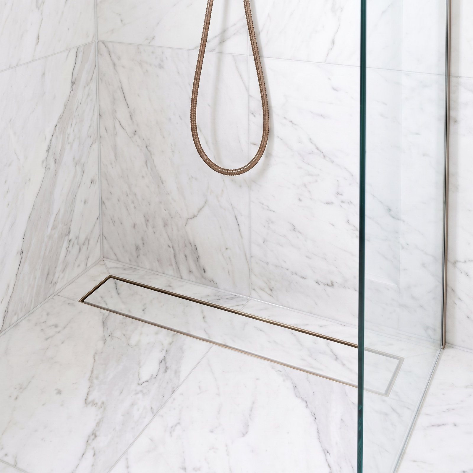 Brushed bronze linear tile insert drain installed in a white marble shower