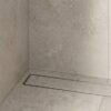 Neston Brushed Stainless Linear Tile Insert Drain In Shower Brushed stainless steel linear tile insert drain installed along a stone-tiled shower wall