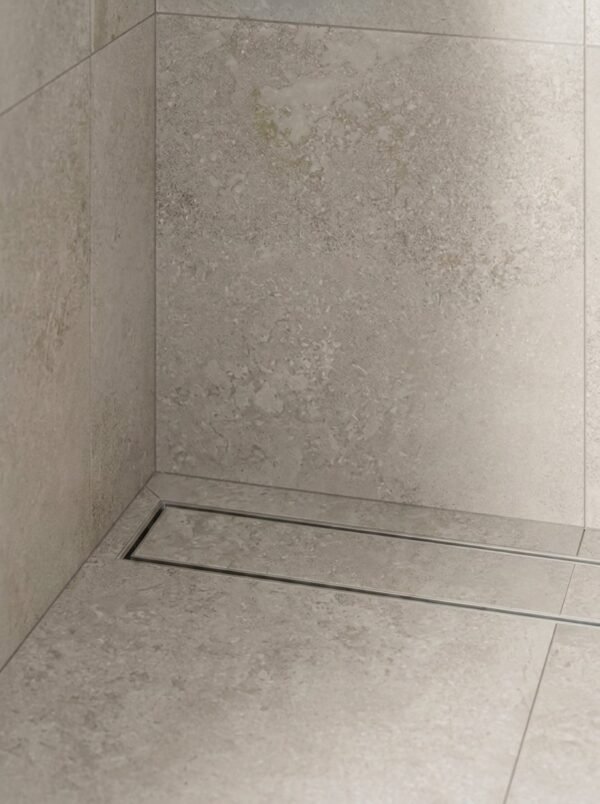 Neston Brushed Stainless Linear Tile Insert Drain In Shower Brushed stainless steel linear tile insert drain installed along a stone-tiled shower wall